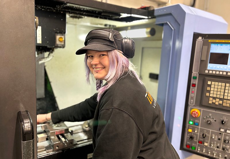 Kvinnlig cnc-tekniker med hörselkåpor står vid arbetsmaskin