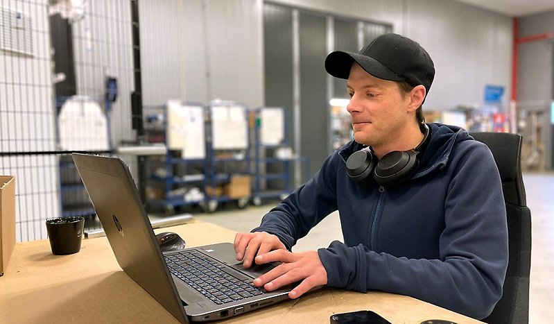 Man i keps och blå tröja sitter framför sin dator