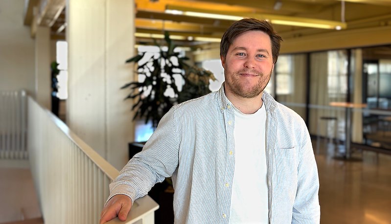 Man står i kontorslandskap och tittar leende in i kameran