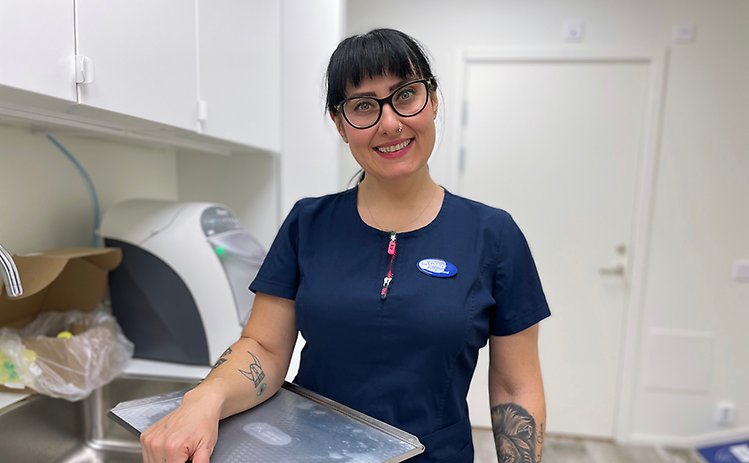 En kvinna med mörkt hår och glasögon som står i ett rum med en bricka i ena handen.