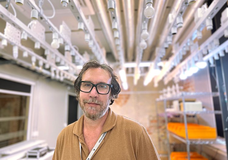 Man med grått hår och glasögon och brun pikétröja står i fabrik.